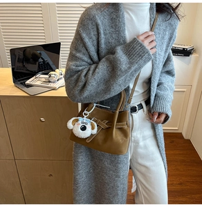 Gros plan du sac seau en daim marron avec sangles croisées et breloque en forme de chien peluche