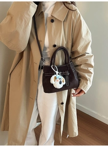 Détail d'un sac seau en daim marron foncé avec bandoulière réglable et breloque chiot peluche