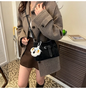 Détail du sac en daim noir avec surpiqûres blanches et porte-clés en peluche chien mignon