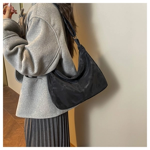 Side view of black matte suede hobo bag worn by model over a grey wool coat