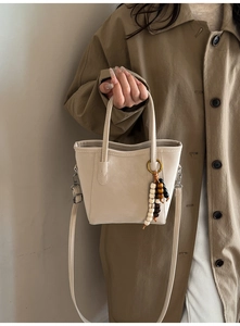 Detail of cream leather bucket bag with wooden bead pendant and slim shoulder strap