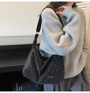 Close-up of black hobo shoulder bag with matte finish and logo on grey knit sweater