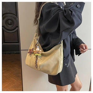 Beige hobo bag with teddy bear charm shown on a shoulder in a modern indoor setting