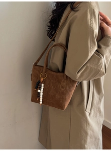 Detail of dark brown suede tote bag with beaded charm and adjustable strap on a coat
