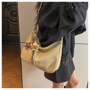 Close-up of khaki crescent tote bag with star and bear charms on a shoulder strap