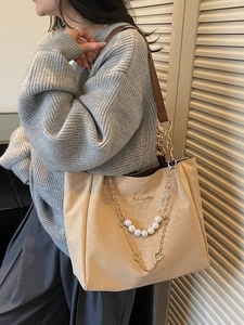 Beige tote bag with pearl chain and leather straps, shown on model's shoulder