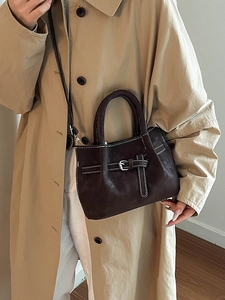 Sac à main en cuir marron foncé avec surpiqûres blanches et boucle argentée sur trench kaki