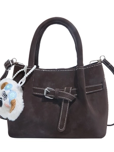Sac à main en daim marron foncé avec sangle décorative et breloque en peluche sur fond blanc