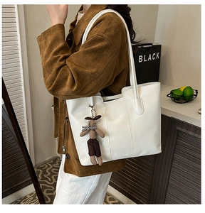 Detail view of large white leather tote bag with brown rabbit charm and long straps