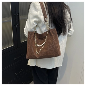 Detail of leopard print tote bag featuring pearl beads, gold chains, and clover charm
