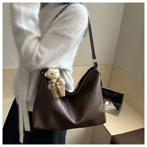 Detail of dark brown leather tote bag with a cute bear charm on a textured surface