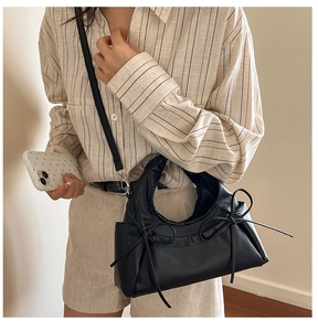 Close-up of black crossbody dumpling bag with ribbon bows and matte leather texture