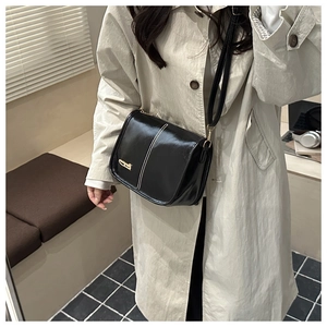 Détail de sac bandoulière noir avec coutures blanches sur trench-coat beige porté