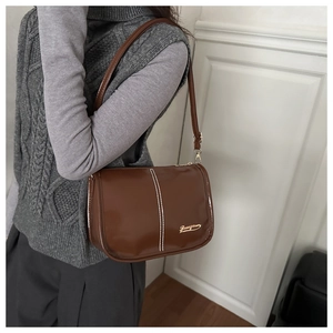 Détail d'un sac à bandoulière en similicuir marron foncé avec surpiqûres et logo métal