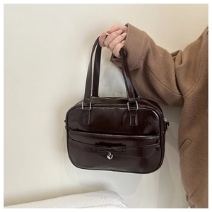 Detail of a chocolate brown glossy leather handbag featuring a bow and heart pendant