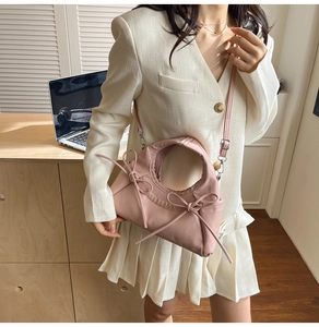Pink fabric dumpling bag with side ribbons and shoulder strap worn by a model