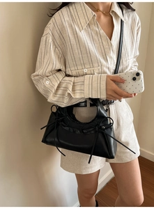 Detail of a black chic crossbody bag with stylish side bow ribbons and a textured finish