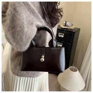 Détail d'un sac bandoulière marron foncé brillant avec pendentif décoratif en métal doré