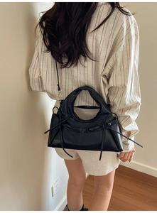 Detail of black crossbody bag featuring long ribbon bows and detachable strap on model