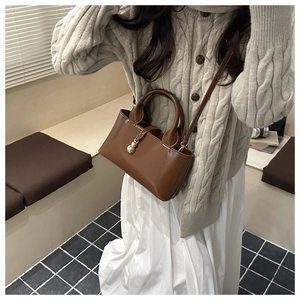 Détail du sac seau marron foncé brillant avec breloques dorées et texture en cuir