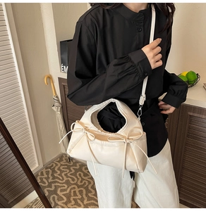 Detail view of a cream-colored puffy crossbody bag with elegant side bow accents