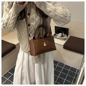Detail of caramel brown handbag featuring a decorative gold gourd-shaped metal charm