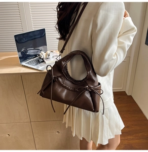 Detail of side bow decoration and pleated handle on dark brown PU leather handbag