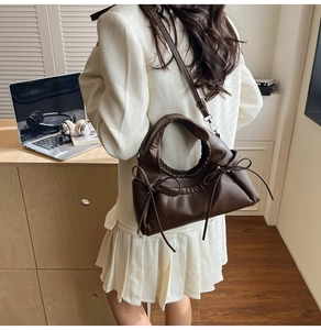 Detail view of dark coffee crescent bag with bow accents worn with a white blazer