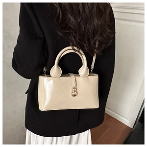 Détail d'un sac à main en cuir verni beige avec breloque dorée porté sur un manteau noir