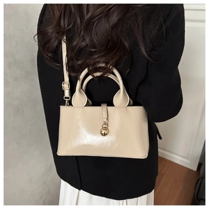 Detailed back view of a beige patent leather handbag worn as a stylish crossbody bag