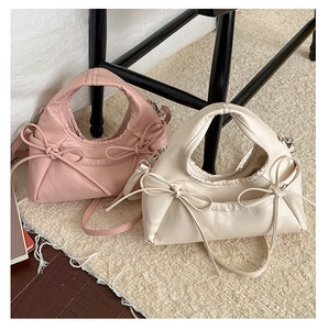 Detailed view of two bow-accented pleated handbags in soft pink and cream white colors