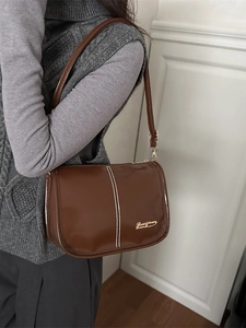 Brown retro PU shoulder bag with white stitching and gold logo worn on a grey vest