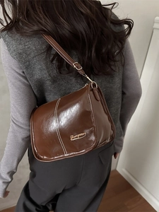 Brown vintage faux leather crossbody bag with white stitching and gold lettering detail