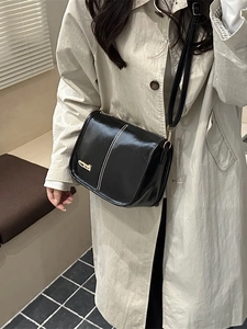 Chic black glossy shoulder bag with white stitching shown on beige trench coat model