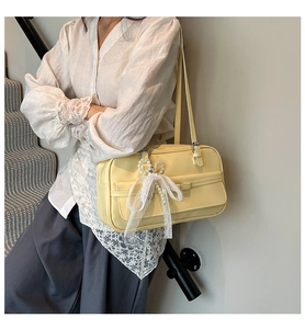 Detail of light yellow underarm bag with white lace bow and pearl pendant on a model