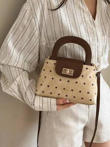 Elegant polka dot handbag with top handle and gold twist lock shown on casual outfit