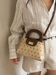 Chic beige canvas polka dot handbag with brown leather flap and gold lock shown on shoulder