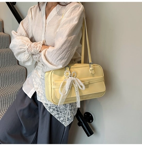 Detail of yellow baguette bag with pearl and lace bow charms on a woman's shoulder