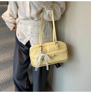 Detail of light yellow underarm bag featuring lace bow and pearl heart charm accessories