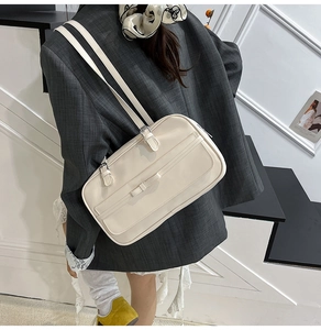 Detail of cream white Boston shoulder bag with slim buckle and bow on a model