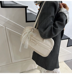 Close-up of cream PU leather handbag featuring bow detail and pearl lace charm pendant