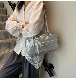 Close-up of silver shoulder bag featuring pearl bow and lace charms on stairs