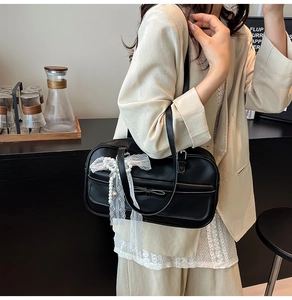 Close-up of black shoulder bag featuring white lace bow and pearl charm detail