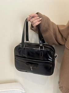 Minimalist black glossy bowling bag with a bow accent and top handles shown in hand