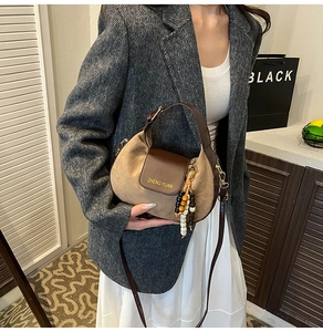 Detail of khaki suede crossbody bag with brown leather flap and beaded charm