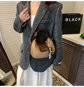 Detailed view of crescent shoulder bag featuring matte brown leather and beaded charm accessory