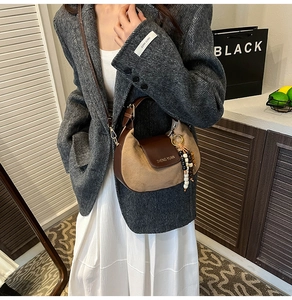 Detail of a brown patchwork half-moon bag with elegant beaded tassel and suede texture