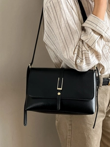Sac à bandoulière en cuir noir avec boucle dorée porté par un mannequin en chemise