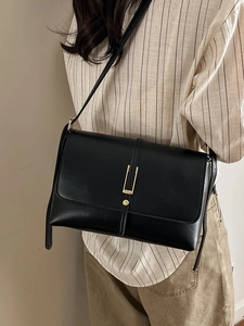 Sac bandoulière vintage en cuir noir avec boucle dorée, porté par un mannequin en tenue