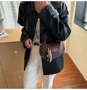 Close-up of brown suede crossbody bag with elegant wooden bead charm and flap detail